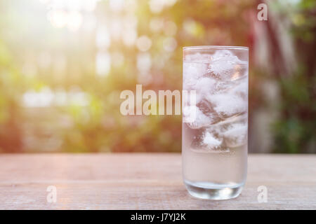 Close up glass of cold water with ice on table with blur nature garden background Stock Photo