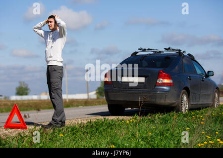 Brunet stands on road near broken car in afternoon Stock Photo