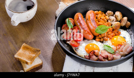 Full English breakfast with fried eggs, sausages, bacon, beans, toasts and coffee. Stock Photo