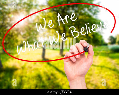 Man Hand writing We Are What We Believe with black marker on visual screen. Isolated on background. Business, technology, internet concept. Stock Phot Stock Photo