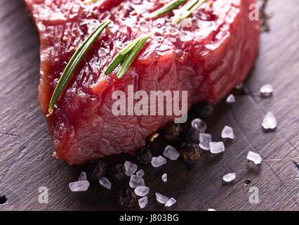 Beef steak with rosemary , salt and pepper on a old wooden table . Stock Photo