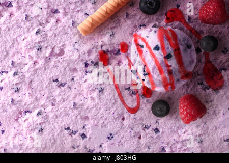 Ice cream flavored berries texture background with ball. Garnished with blueberries and raspberries and syrup. Top view. Horizontal composition. Stock Photo