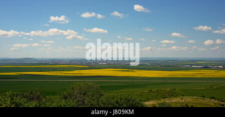 The oil refinery among the yellow rapeseed fields on the background of the Balkan Mountains, modern technologies of people and the nature in the sprin Stock Photo