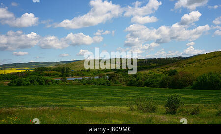 The green wheat field on the background of a pond and yellow rapeseed fields, the beautiful view on a valley among the Balkan mountains in spring.