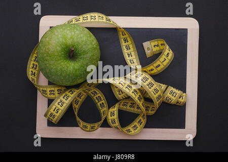 Measuring tape on blackboard with green apple. Black background. Diet concept. Stock Photo