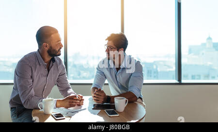 Two businessmen sitting on a coffee table and discussing business matters. Business executives working in their office. Stock Photo