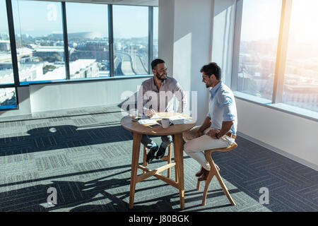 Business partners in happy mood discussing work. Two men sitting at a table in office in a highrise building. Stock Photo