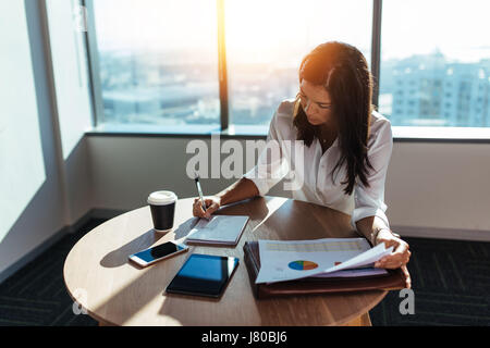 Young woman entrepreneur making business working at coffee table in office. Female business executive making business plans with a coffee cup on her t Stock Photo