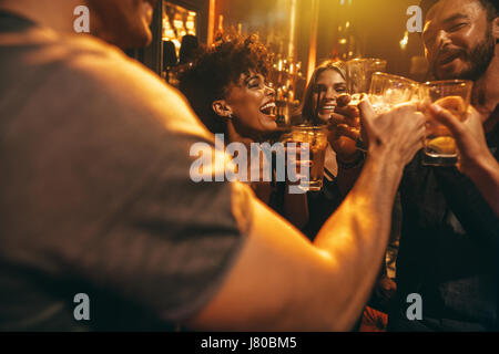 Happy group of people enjoying drinks at bar. Young friends at nightclub toasting cocktails. Stock Photo