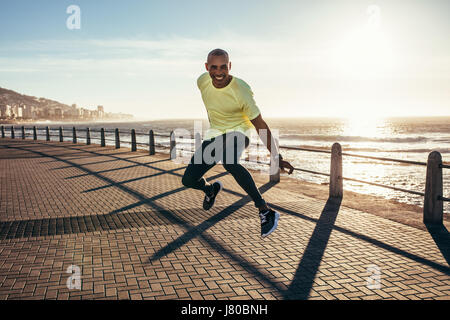 Young african man jumping on a road by the sea. Excited young runner jumping. Stock Photo