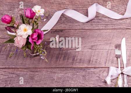 Place table settings with fork and knife, tied with a white satin ribbon, and flowers on an vintage table top view, flat lay, overhead view with space for text Stock Photo