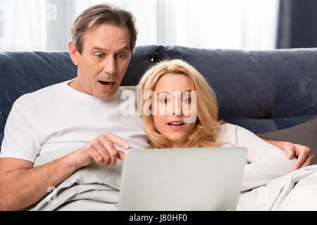 Happy middle aged couple using laptop and lying on bed at home Stock Photo