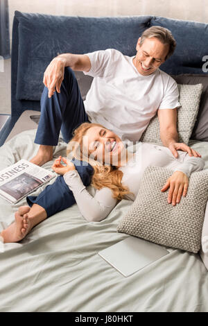 Happy middle aged couple laughing and lying on bed at home Stock Photo