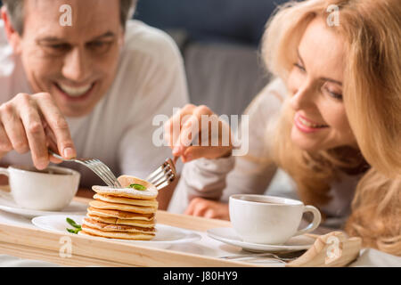 Happy middle aged couple eating pancakes together in bed Stock Photo