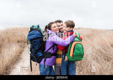 Happy family with backpacks hugging on rural path at cloudy autumn day Stock Photo