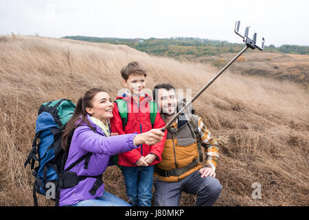 Happy family with backpacks in tall dry grass taking selfie in rural area Stock Photo