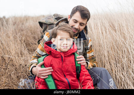 Close-up portrait of smiling father with cute little son sitting in tall dry grass at autumn day Stock Photo