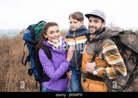 Close-up portrait of smiling family with backpacks standing embracing on rural path Stock Photo