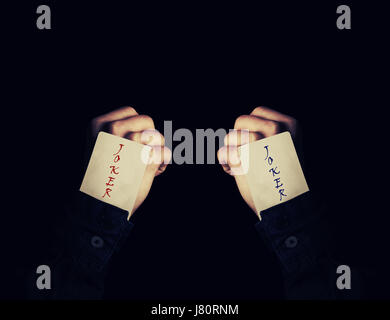 Close up of two fists holding joker playing cards in the sleeve. Magician showing his trick with cards on a black background. Casino game concept. Stock Photo