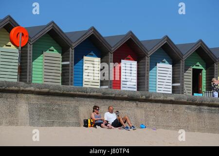 People enjoy the sunshine by the beach huts on Blyth Beach in Northumberland. Britons hoping for a scorching bank holiday may be disappointed as forecasters predict temperatures will start to drop on Saturday with a chance of rain and thunderstorms throughout the long weekend. Stock Photo