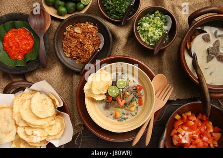 Soto Betawi, popular meat in coconut milk soup from Jakarta. Served with tomato, celery, scallion, shallots, cracker, and lime. Stock Photo
