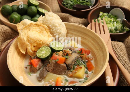 Soto Betawi, popular meat in coconut milk soup from Jakarta. Served with tomato, celery, scallion, shallots, cracker, and lime. Stock Photo