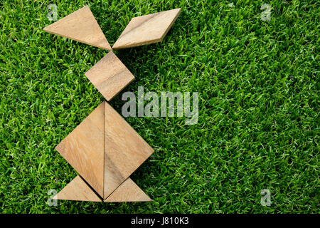 Wooden tangram puzzle in rabbit shape on artificial green grass background (Concept of Happy Easter) Stock Photo