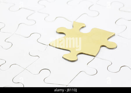 Golden puzzle piece distinguishes from remainder of white puzzle symbolizing solving problems successfully. Stock Photo