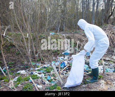 A volunteer man in white protective clothing collects garbage Stock Photo