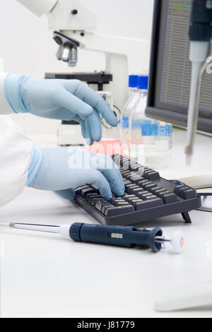 Gloved hands of a white-coated scientist using a computer in a bio-science laboratory Stock Photo