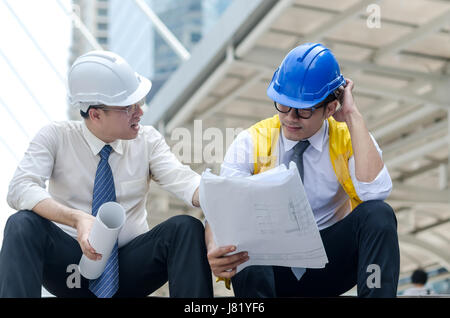 Two asian architects discussing about new project with paperwork at step of business walk way area in the city. Stock Photo