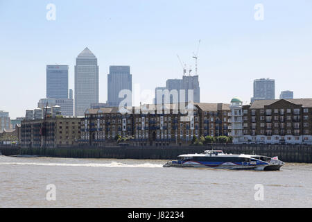 A Thames Clipper river bus travels upstream along the River Thames at Rotherhithe in London, UK. Canary Wharf in the background. Stock Photo