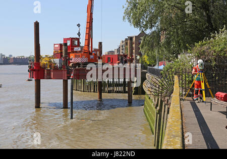 A jack-up barge on the River Thames in east London undertakes work for the Thames Tideway Tunnel project. A surveyor works on the river bank (right) Stock Photo