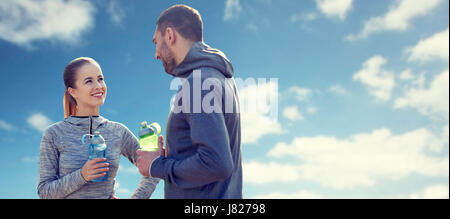 smiling couple with bottles of water over blue sky Stock Photo