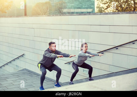 couple doing squats on city street stairs Stock Photo