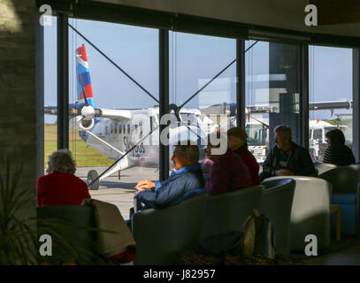 Passenger waiting area with people waiting to board a flight and a plane in the background at Land's End Airport, St. Just, Cornwall, England UK Stock Photo