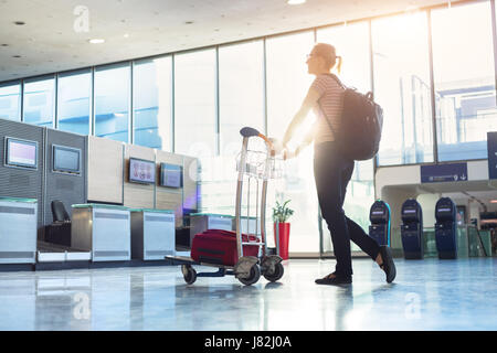 Woman walking with a luggage trolley to a airline check-in counter in a modern airport before an international flight Stock Photo