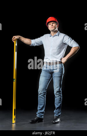 Male engineer in hard hat holding level tool and looking up on black Stock Photo