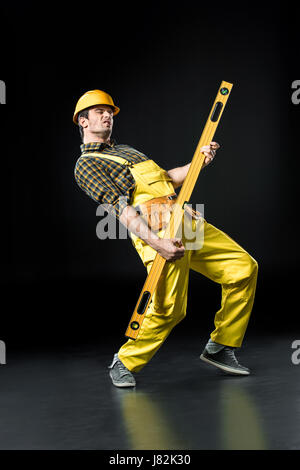 Male construction worker in helmet gesturing with level tool on black Stock Photo