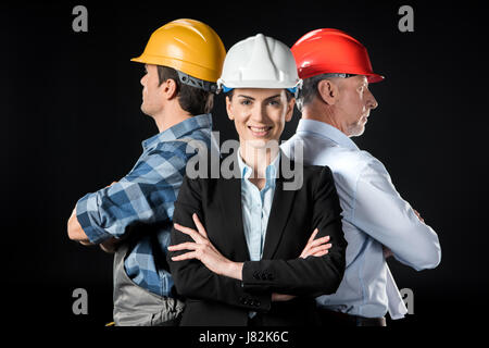 Portrait of two confident architects and engineer in hard hats on black Stock Photo