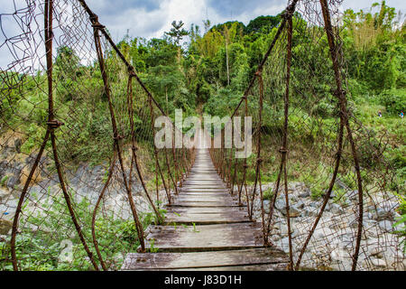 A suspension bridge made of cable, wire fencing and wood hangs over a river in the jungle area of Northern Luzon Island, Philippines. Stock Photo