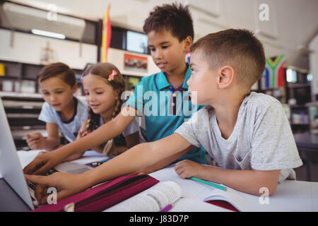 Attentive schoolkid using laptop in library at school Stock Photo