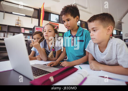 Attentive schoolkid using laptop in library at school Stock Photo