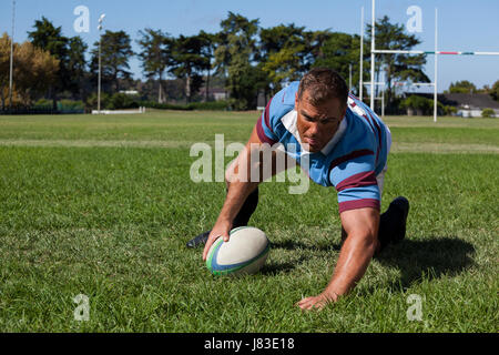 Player holding ball while playing rugby on field during sunny day Stock Photo