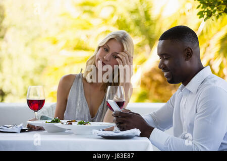 Irritated woman looking at man using phone at table in restaurant Stock Photo