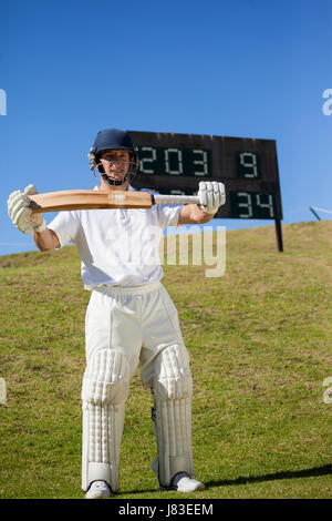 Full length of confident cricketer holding bat while standing on field Stock Photo