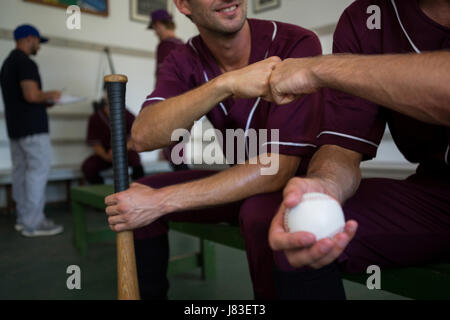 Cropped image of baseball players sitting on bench in locker room Stock Photo