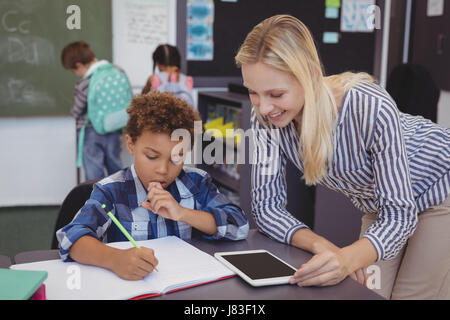 Teacher helping schoolboy with his homework in classroom at school Stock Photo