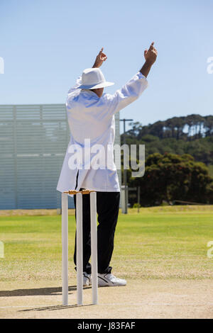 Full length of cricket umpire signalling six runs during match on sunny day against clear sky Stock Photo