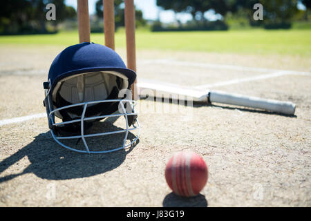 Sports helmet and ball with bat by stumps on pitch during sunny day Stock Photo